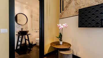 A modern bathroom with a round mirror, a sink with a black basin, a toilet, and a small round table with a potted orchid.