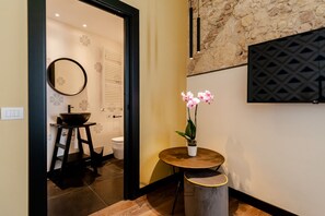 A modern bathroom with a round mirror, a sink with a black basin, a toilet, and a small round table with a potted orchid. - KyS Castello - Suite Villanova (Cagliari)