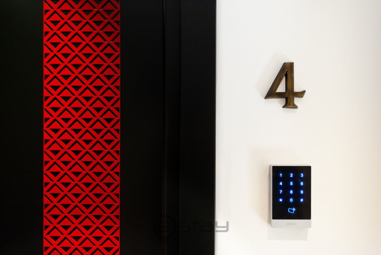 Un ascensor moderno con un patrón geométrico rojo a la izquierda, un número '4' grande a la derecha y un teclado digital debajo.