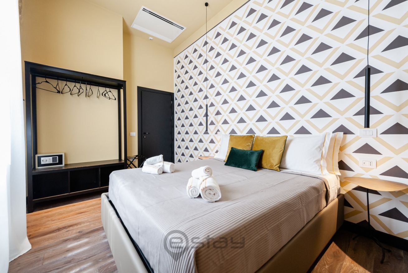 Une chambre d’hôtel comprenant un lit, un climatiseur fixé au mur, une table de chevet et un mur orné d’un motif géométrique.