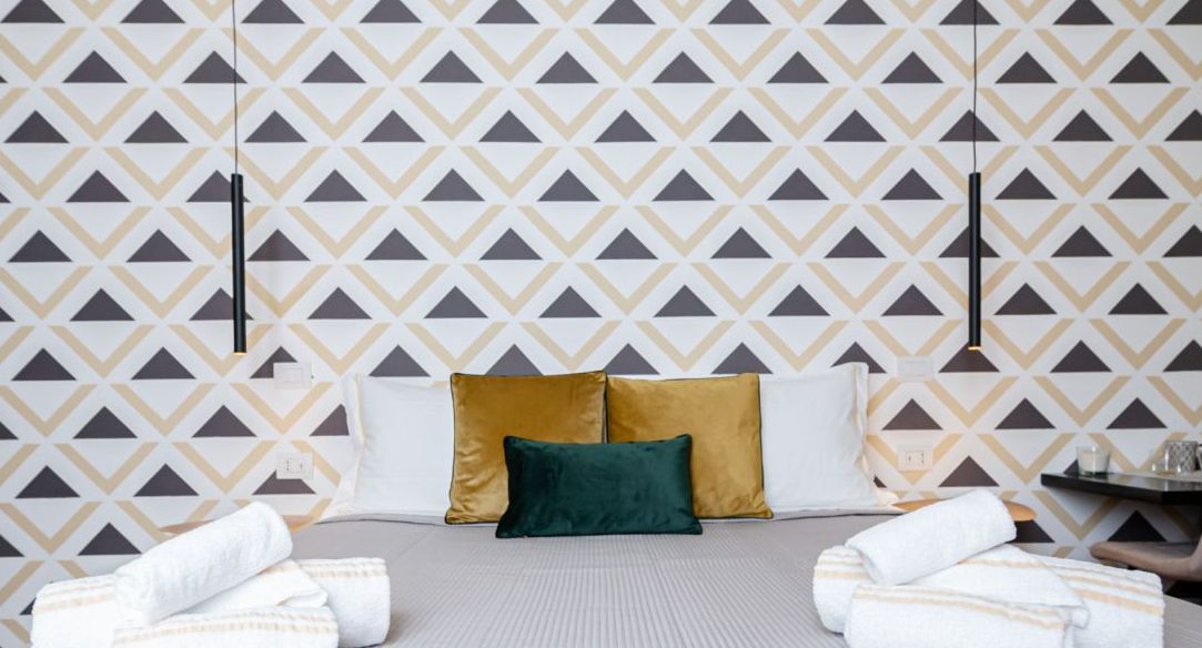 A hotel room with a patterned wallpaper, a bed with two pillows, and towels on the floor.