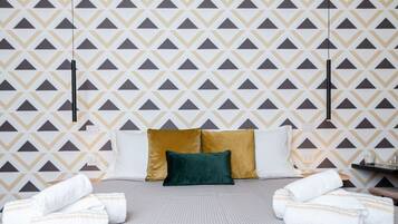 A hotel room with a patterned wallpaper, a bed with two pillows, and towels on the floor.