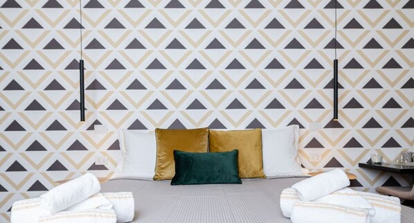 A hotel room with a patterned wallpaper, a bed with two pillows, and towels on the floor. - KyS Castello - Suite Villanova (Cagliari)