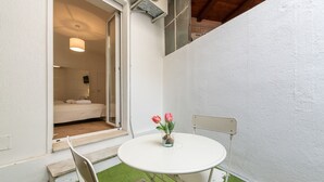 Una stanza piccola con un letto, un tavolo bianco con due sedie e un tavolino con fiori.