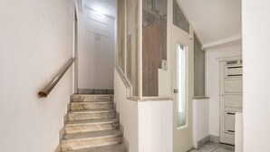 Una scala che conduce a una porta con zanzariera, una parete bianca e un pavimento piastrellato.