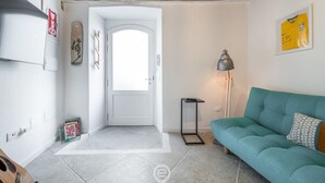 Et værelse med en hvid dør, en turkis sofa, en lampe og et billede i ramme på væggen.