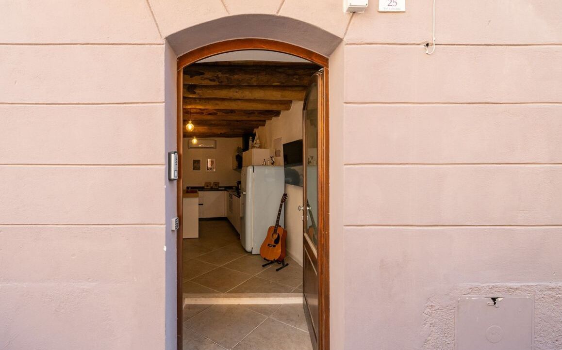 A narrow hallway leading to a kitchen with a guitar leaning against the wall.