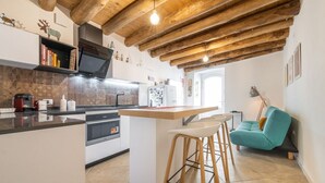 Et moderne køkken med træloft, en central ø med barstole og en teal-sofa i et lyst rum.