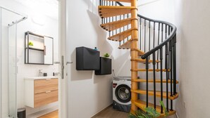 A modern bathroom with a wooden spiral staircase, a washing machine, and a minimalist design. - Saturnino - Apartment (Cagliari)
