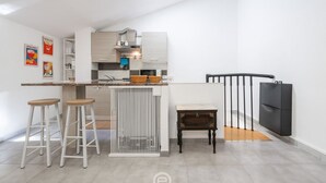 A modern kitchen with a central island, bar stools, a small table, and a black chair. - Saturnino - Apartment (Cagliari)