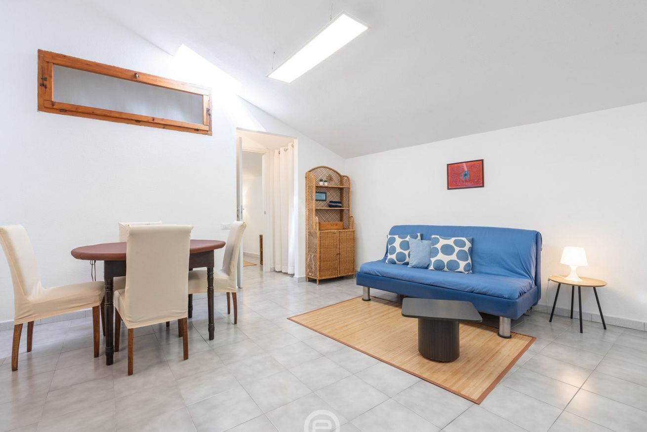 Un salon avec un canapé bleu, une table à manger avec des chaises, un meuble en bois et un tableau encadré au mur.