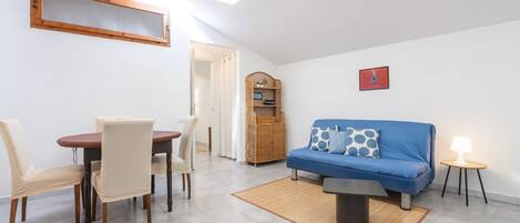 Un salon avec un canapé bleu, une table à manger avec des chaises, un meuble en bois et un tableau encadré au mur.
