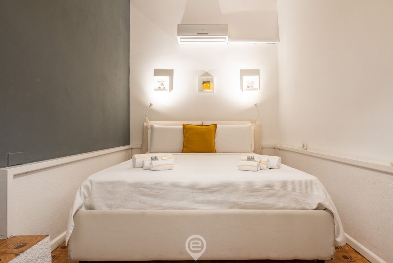 A neatly arranged hotel room with a large bed, a bedside table, and a wall-mounted air conditioner.
