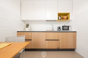 Una cocina compacta con armarios blancos, un microondas, una cafetera y un estante amarillo con utensilios de cocina.