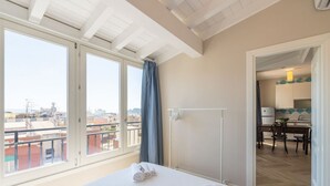 Une chambre d’hôtel avec un lit, une fenêtre avec des rideaux, une vue sur la ville et une kitchenette dans la pièce adjacente.