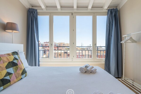 Une chambre d’hôtel avec un lit, une lampe, une fenêtre avec des rideaux et une vue sur des immeubles.