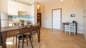 Une cuisine de taille réduite avec des meubles blancs, une table à manger en bois et un parquet disposé en motif chevron.