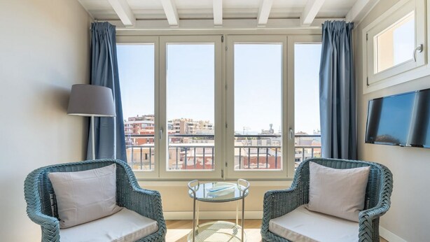 Un balcon avec des fauteuils en osier, une table en verre et un téléviseur fixé au mur.