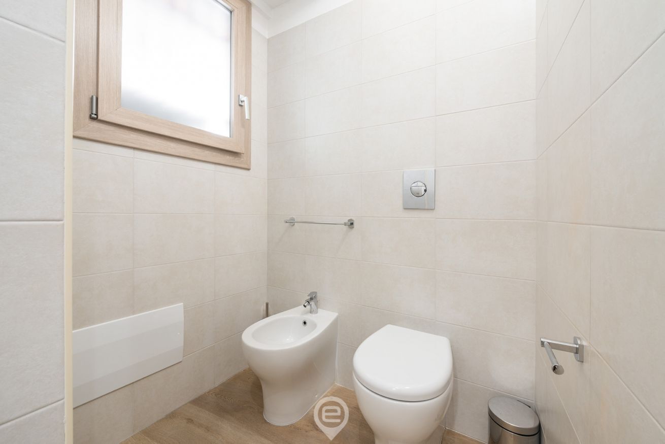 A small, modern bathroom with a bidet, toilet, and a window.