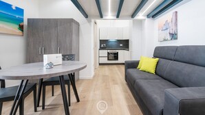 Un espace de vie compact comprenant une table à manger, un canapé, un coin cuisine et un tableau au mur.