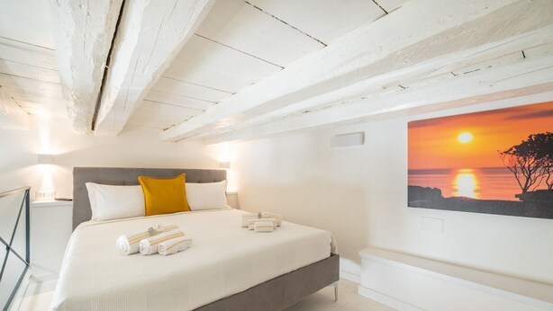 Une chambre à coucher avec un lit, un tableau représentant un coucher de soleil et un plafond blanc.