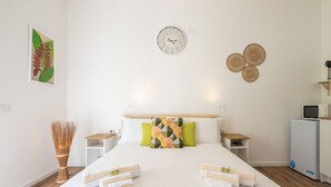 A neatly arranged hotel room with a large bed, a wall clock, and a small desk with a computer.