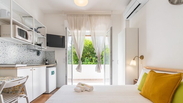 Ein Hotelzimmer mit einem Bett, einer kleinen Küchenzeile, einem Fernseher und einem Fenster mit Vorhängen.