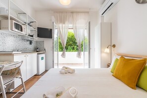 Une chambre d’hôtel avec un lit, une petite kitchenette, une télévision et une fenêtre avec des rideaux.