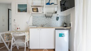 Eine kompakte Küche mit weißen Schränken, einer Mikrowelle, einem kleinen Kühlschrank und einem Spülbecken. Ein Tisch mit Stühlen und ein Bild an der Wand.