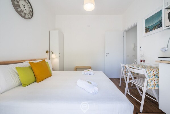 Une chambre d’hôtel avec un lit, un bureau, une chaise, une horloge et un tableau au mur.