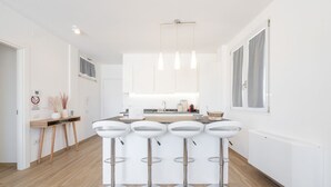 Una cucina moderna con mobili bianchi, un'isola centrale con sgabelli da bar, illuminazione a sospensione e una finestra con tende.