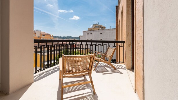 Ein Balkon mit zwei Korbstühlen und einem schwarzen Metallgeländer.