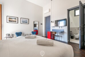 Une chambre d’hôtel moderne dotée d’un grand lit, d’un téléviseur fixé au mur, d’un bureau avec une chaise et d’une petite kitchenette.
