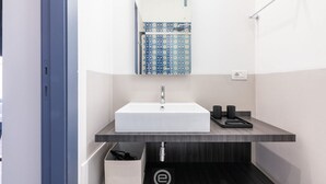 Ein modernes Badezimmer mit einem weißen Waschbecken, einem dunklen Holz-Waschtisch und einer blauen Duschkabine mit Muster.
