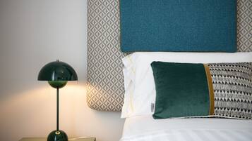 A neatly made bed with patterned pillows, a green lamp on a bedside table, and a patterned wall behind the bed.