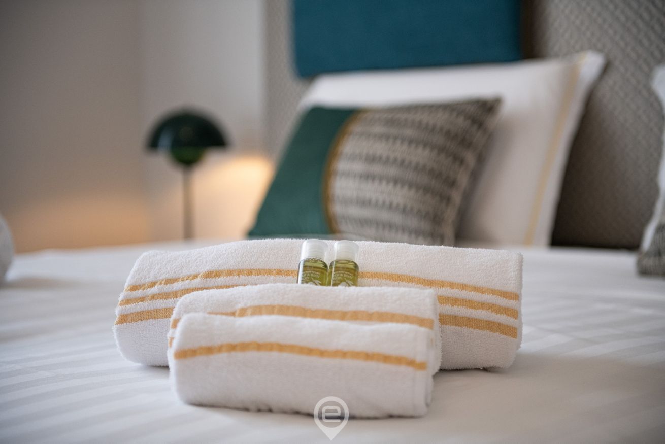 Un lit bien fait, avec des serviettes à rayures et une bouteille de lotion.