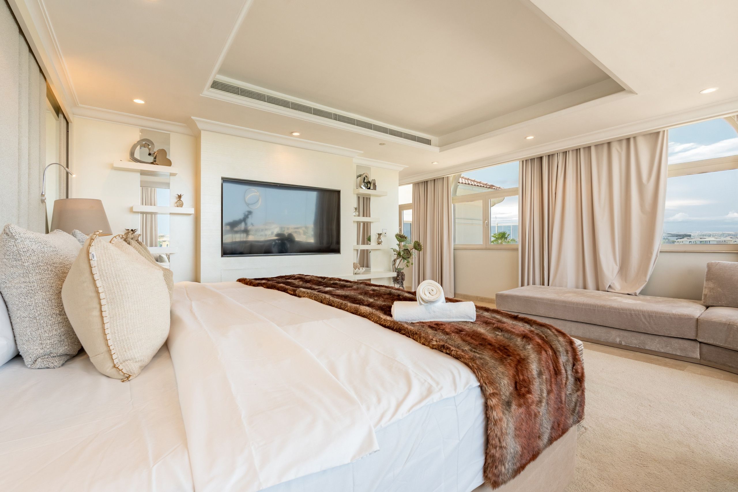 Een moderne hotelkamer met een groot bed, een flatscreen televisie, een bank en uitzicht op de stad.