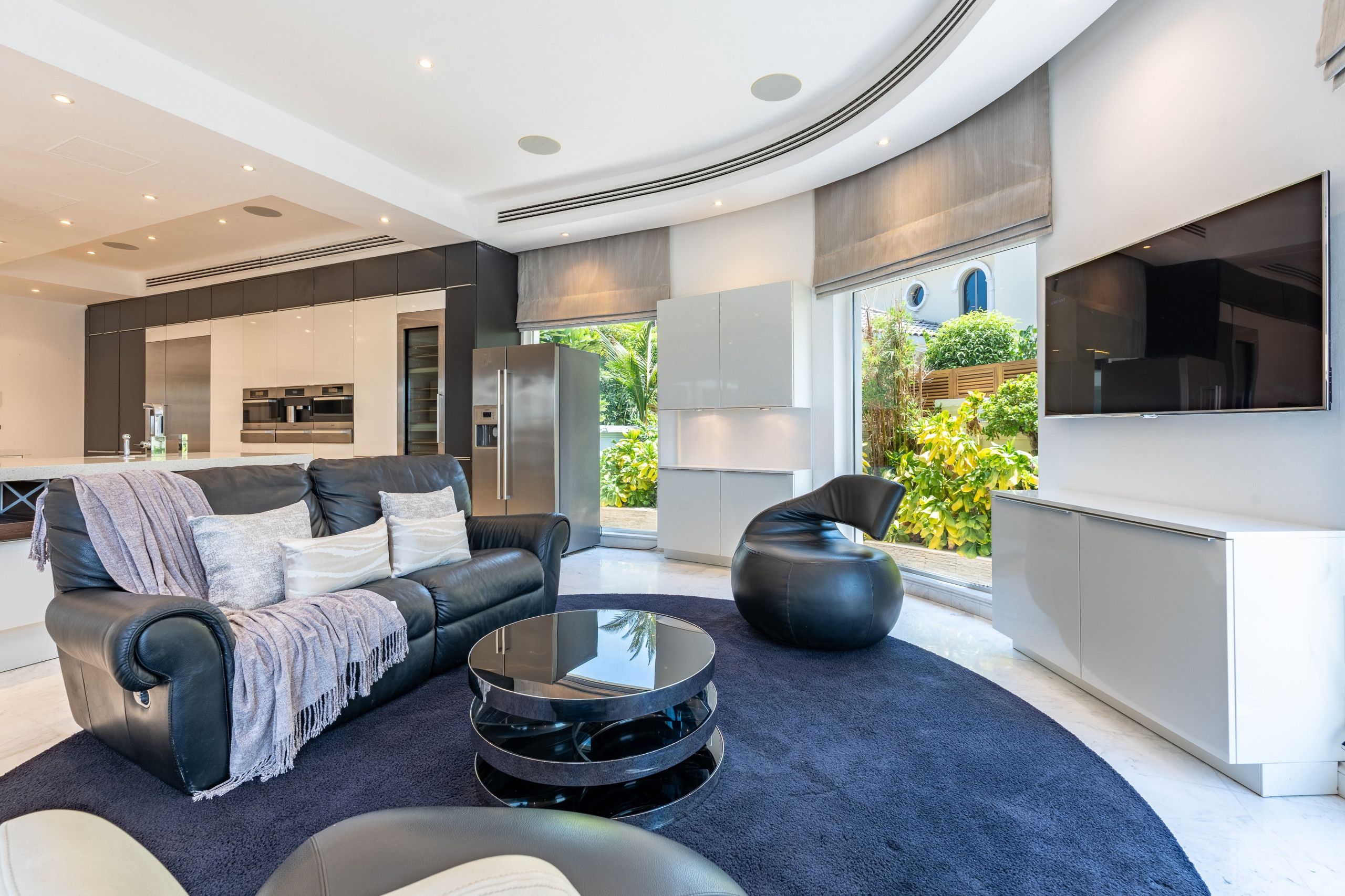 Un salon moderne avec un canapé en cuir noir, une table basse en verre et un fauteuil en forme de poire noir.