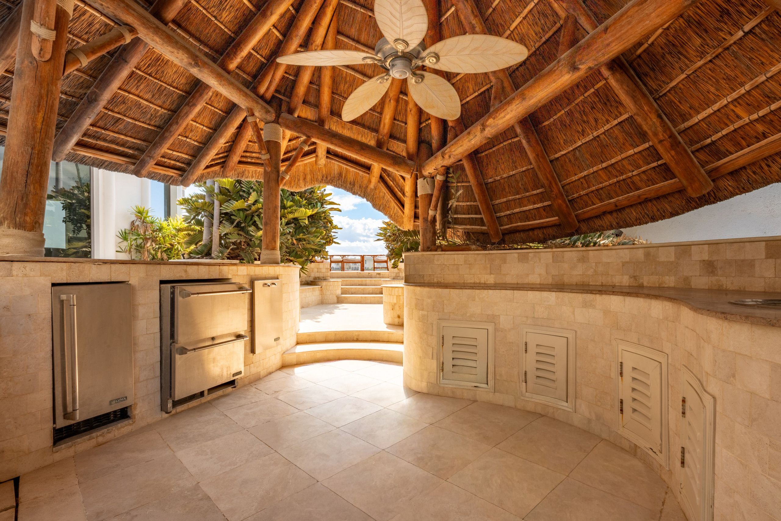 Un área de cocina exterior techada con ventilador de techo, electrodomésticos integrados y vista al océano.