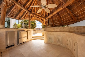 A covered outdoor kitchen area with a ceiling fan, built-in appliances, and a view of the ocean.