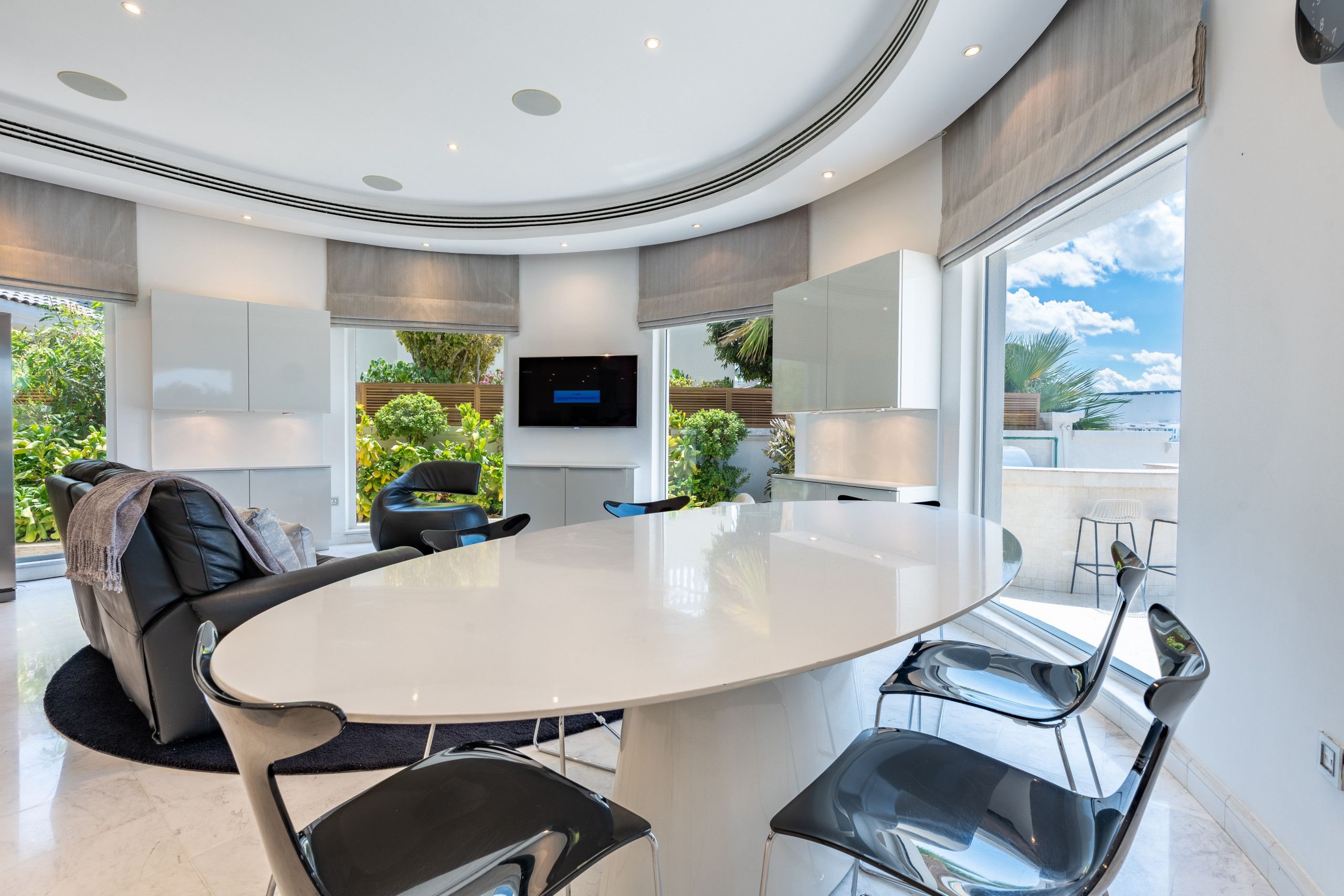 Ein modernes Interieur mit einem runden Tisch, schwarzen Stühlen, einem Flachbildfernseher und Blick ins Grüne.