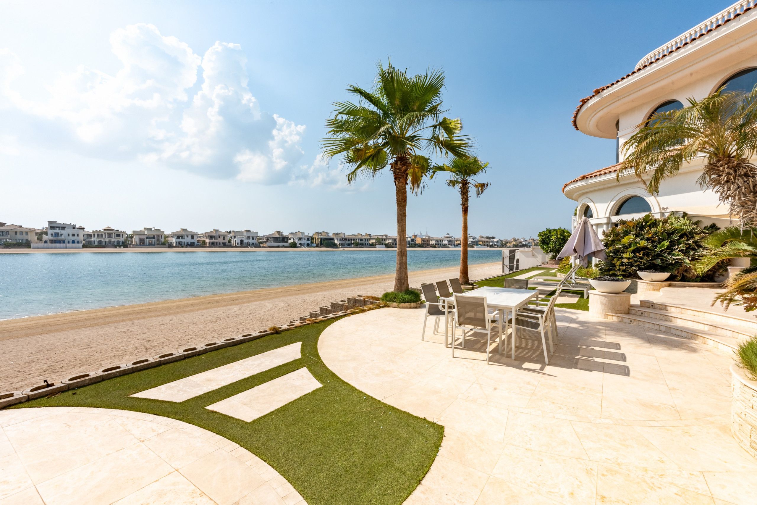 A beachfront property with a patio area, palm trees, and a view of the sea.