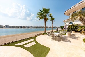 Een pand aan het strand met een terras, palmbomen en uitzicht op zee.