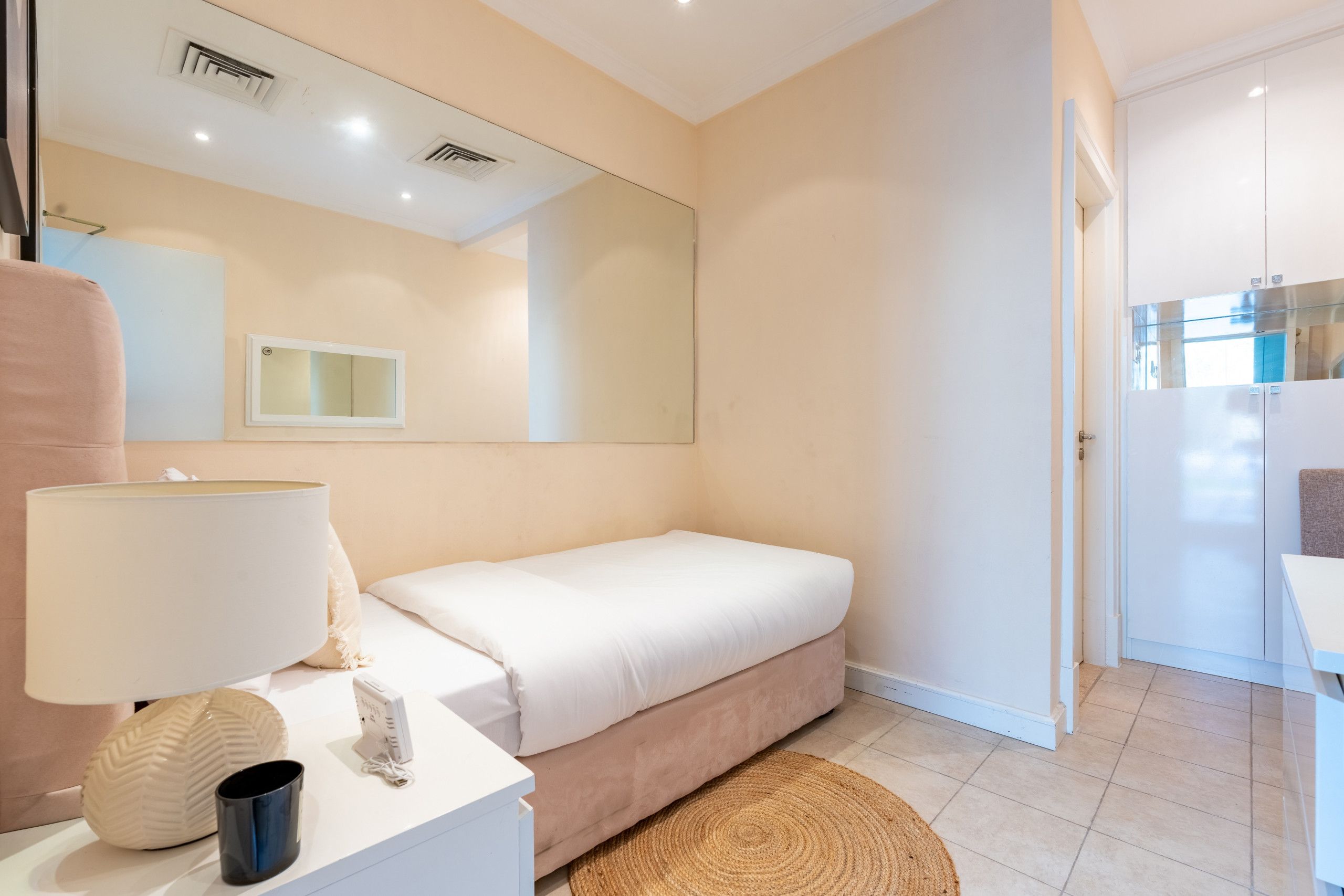Een slaapkamer met een bed, een nachtkastje met een lamp, een spiegel en een deur die naar een andere kamer leidt.