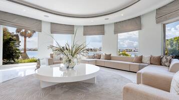 A modern living room with a central coffee table, a sofa set, and large windows with views of the sea.