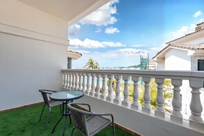 Een balkon met een tafel en twee stoelen, met uitzicht op een kustgebied met gebouwen en een heldere lucht.