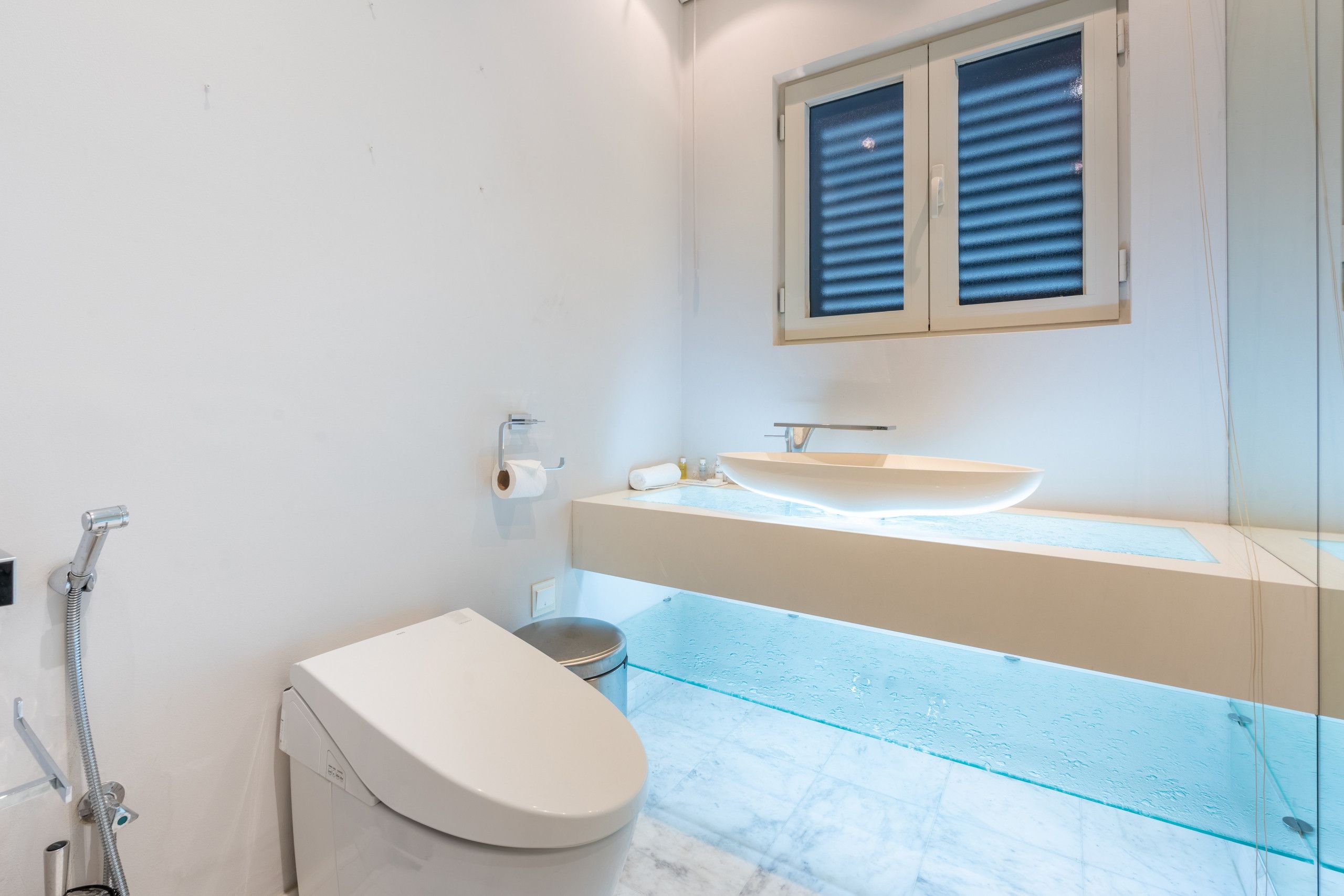 Een moderne badkamer met toilet, een wastafel met glazen ombouw en een douche.