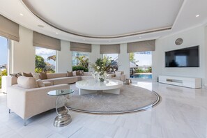 Ein modernes Wohnzimmer mit gewölbter Decke, einem Ecksofa, einem Glastisch und einem großen Fernseher.