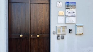 A wooden double door with a brass handle, a wall-mounted mailbox, a doorbell, a security intercom, and a plaque with the number 17. - Affittacamere Carmè - Suite Porto Conte (Alghero)