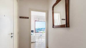 Un couloir menant à une chambre dotée d’une grande fenêtre, d’un miroir et d’une porte avec un interrupteur.